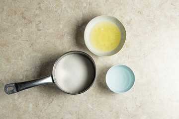 Top-view shot of basic baking ingredients on a marble countertop: sugar in a metal pan, beaten eggs in a white bowl, and an empty light blue bowl. Clean, minimalist food styling, perfect for recipe tu