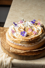  A beautifully baked meringue cake adorned with edible violet and pansy flowers sits on a wooden board lined with parchment paper. Rustic yet elegant presentation perfect for dessert menus or food blo