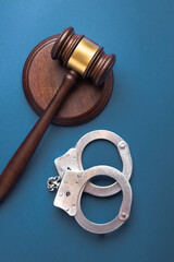Judge gavel and handcuffs on a blue surface. Symbolizes courtroom authority and enforcement. Top...