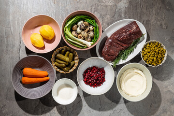 A neatly arranged collection of ingredients for a classic salad: boiled potatoes, carrots, quail eggs with green onions, pickles, green peas, frozen cranberries, mayonnaise, salt, and a piece of raw b