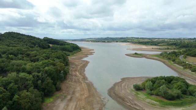 Aerial view of a reservoir surrounded by verdant forests and exposed shorelines under a cloudy sky, Matlock, England, United Kingdom.