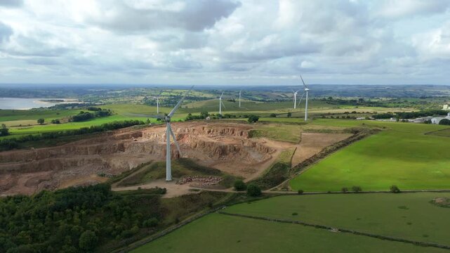 Aerial view of wind turbines standing tall amidst a quarry and vibrant green fields, under a cloudy sky, Matlock, England, United Kingdom.