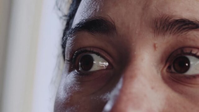 Extreme close up of a woman's expressive brown eyes. Her pupils dilate and her gaze darts around, conveying a sense of fear and paranoia