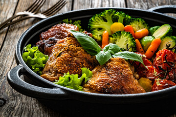 Roasted chicken thighs and vegetables in cast iron pan on wooden table	