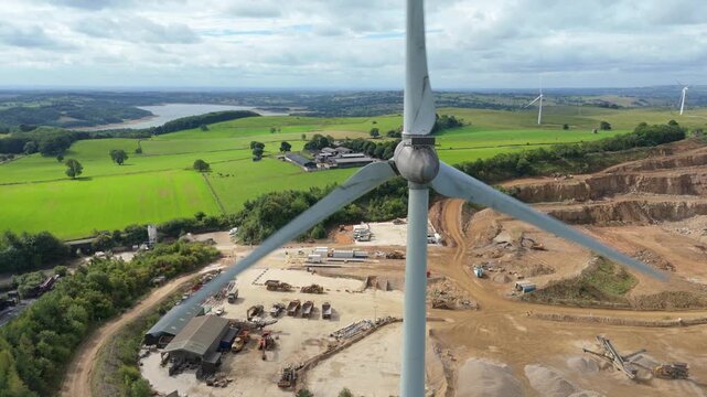 Aerial view of wind turbines stand tall besides a vast quarry contrasting with the lush green fields and a distant reservoir, Matlock, England, United Kingdom.