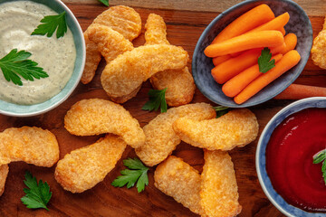 Chicken nuggets with fresh vegetables and dips, on a wooden board, overhead flat lay shot, a close-up