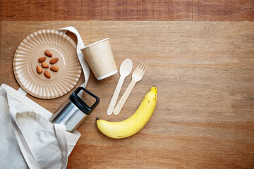 Eco-friendly picnic setup with reusable cutlery, paper cup, stainless bottle, banana, and almonds on wooden background. Perfect for zero waste, healthy lifestyle, and sustainability concepts.