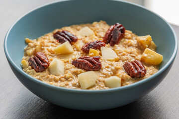 creamy pumpkin oatmeal topped with fresh apple slices and caramelized pecans