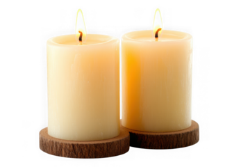 Two lit cream pillar candles on dark wood coasters against black background flame burning