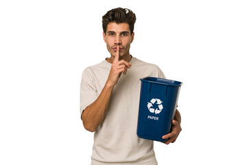 Young caucasian man holding a paper trash for recycle keeping a secret or asking for silence.