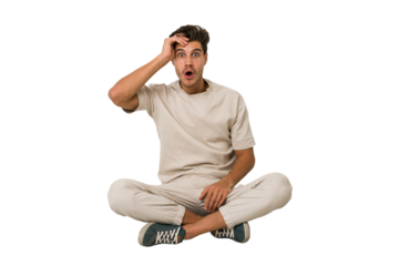 Young caucasian man sitting on the floor isolated on white background shouts loud, keeps eyes opened and hands tense.