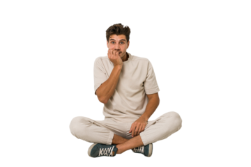 Young caucasian man sitting on the floor isolated on white background biting fingernails, nervous and very anxious.