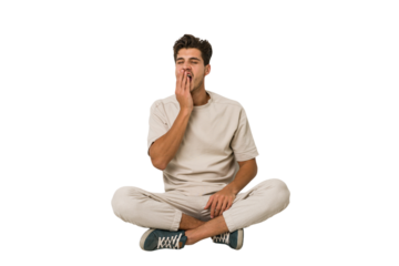 Young caucasian man sitting on the floor isolated on white background yawning showing a tired gesture covering mouth with hand.