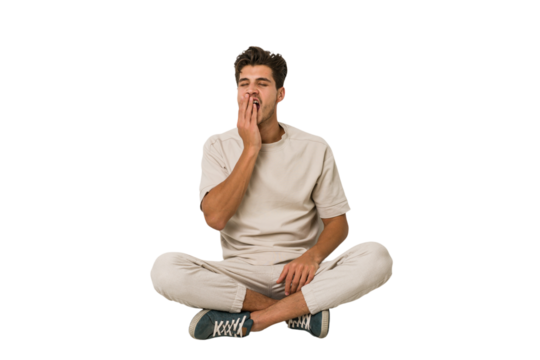 Young caucasian man sitting on the floor isolated on white background yawning showing a tired gesture covering mouth with hand.