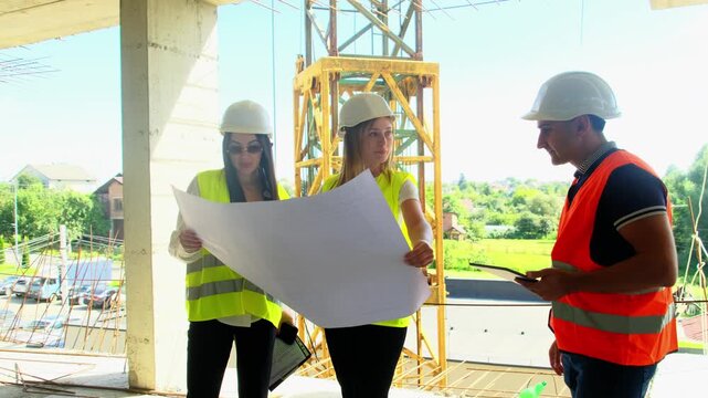 Construction team with helmets review architectural plans at building site. Engineers and taskmaster checks project progress with blueprint indoors