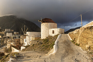 Traditional white windmills on a hillside village at sunset, illuminated path with mountain landscape in the background. in Olympos, Karpathos, Greece,
