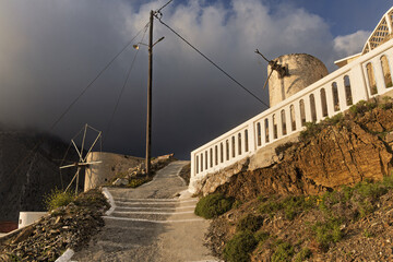 Traditional white windmills on a hillside village at sunset, illuminated path with mountain landscape in the background. in Olympos, Karpathos, Greece,
