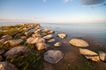 A tranquil scene of a rock beach with wet stones during sunrise, offering a path to the water's edge.