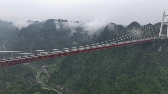 Aerial view of the Aizhai Bridge, a red suspension bridge amidst lush green mountains shrouded in mist, Aizhai Bridge, Hunan, China.