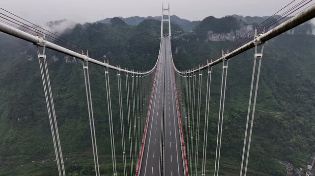 Aerial view of the Aizhai Bridge, a symphony of steel and concrete piercing through the misty, verdant mountains, a testament to human engineering, Aihzai, Hunan, China.