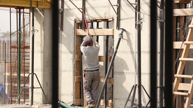 Construction workers secure rebar cages on a developing building site. A large tower crane assists lifting materials for high-rise concrete structure development and infrastructure work.
