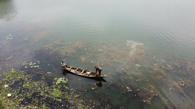 Abuja, Nigeria - 10 October 2025: Aerial view of boat carrying two people on Alex Ekwueme Way, surrounded by green aquatic plants and murky water.