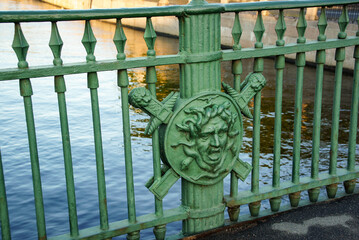 emblem of Medusa’s head. A green metal bridge fence adorned with a decorative emblem of Medusa’s head, a mythical creature from Greek mythology. For architectural studies, decorative purposes