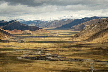Tibet aerial view Expansive landscape of the Tibetan Plateau with snow-capped mountains and arid valleys under dramatic skies. Remote wilderness at the roof of the world 