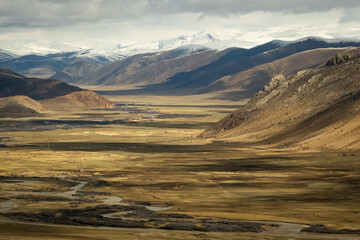 Tibet aerial view Expansive landscape of the Tibetan Plateau with snow-capped mountains and arid valleys under dramatic skies. Remote wilderness at the roof of the world 