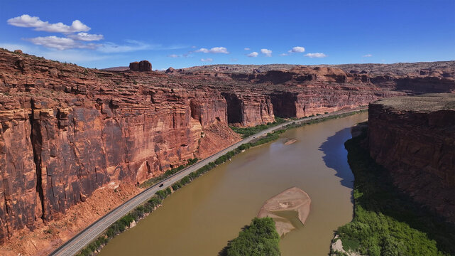 Aerial view of the muddy river snaking between towering red rock cliffs under a vast blue sky, Moab, Utah, United States.