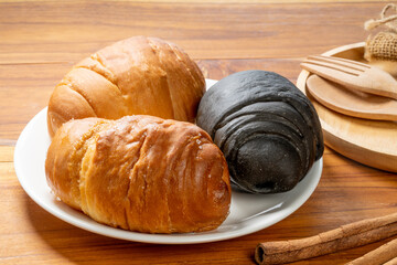Salt bread and charcoal bread on white plate. Freshly baked Japanese-style rolls with golden crust and black charcoal dough, delicious bakery concept on wooden table.
