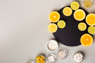 Various nutritional supplements, vitamins and minerals, pills and tablets, citrus fruits - lemon, orange and lime on black stone desk on grey background from above. Natural vitamins from fruits