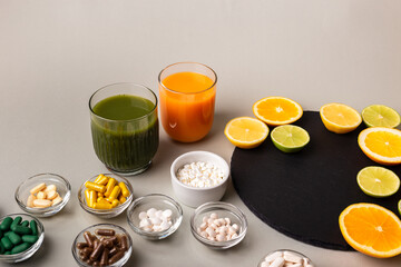 Nutritional supplements, various vitamins and minerals, pills from above on a black stone desk on green background. Smoothie, citrus fruits - lemon, orange and lime as a source of natural vitamins.