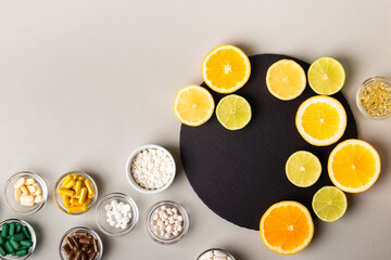 Various nutritional supplements, vitamins and minerals, pills and tablets, citrus fruits - lemon, orange and lime on black stone desk on grey background from above. Natural vitamins from fruits