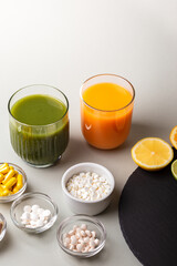 Nutritional supplements, various vitamins and minerals, pills from above on a black stone desk on green background. Smoothie, citrus fruits - lemon, orange and lime as a source of natural vitamins.