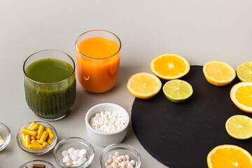 Nutritional supplements, various vitamins and minerals, pills from above on a black stone desk on green background. Smoothie, citrus fruits - lemon, orange and lime as a source of natural vitamins.