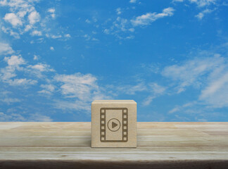Play button with movie flat icon on wood block cube on wooden table over blue sky with white clouds, Business cinema online concept
