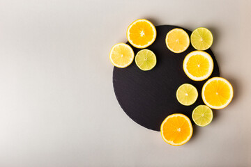 Citrus fruits - lemon, orange and lime on black stone desk on grey background from above. Healthy sweets. Natural vitamins from fruits