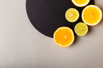 Citrus fruits - lemon, orange and lime on black stone desk on grey background from above. Healthy sweets. Natural vitamins from fruits