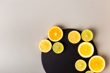 Citrus fruits - lemon, orange and lime on black stone desk on grey background from above. Healthy sweets. Natural vitamins from fruits