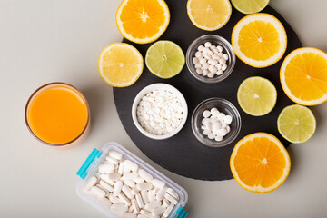 Nutritional supplements, various vitamins and minerals, pills from above on a black stone desk on green background. Smoothie, citrus fruits - lemon, orange and lime as a source of natural vitamins.