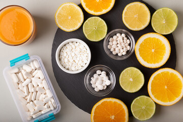 Nutritional supplements, various vitamins and minerals, pills from above on a black stone desk on green background. Smoothie, citrus fruits - lemon, orange and lime as a source of natural vitamins.