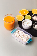 Nutritional supplements, various vitamins and minerals, pills from above on a black stone desk on green background. Smoothie, citrus fruits - lemon, orange and lime as a source of natural vitamins.
