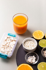 Nutritional supplements, various vitamins and minerals, pills from above on a black stone desk on green background. Smoothie, citrus fruits - lemon, orange and lime as a source of natural vitamins.