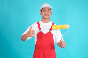 Cheerful Asian Painter Gives Thumbs Up While Holding Roller Brush Against Blue Background