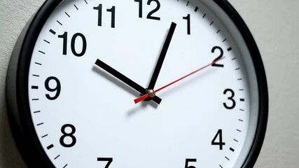 A close-up of a round wall clock with black hands on a white face. A red second hand is visible