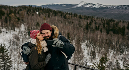 Traveling young woman and man in outwear embracing and taking selfie against mountains