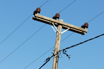 Wooden utility pole with electrical wires against blue sky.
