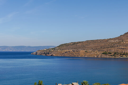 A serene coastal landscape featuring calm blue waters, a rocky shoreline, and a clear sky