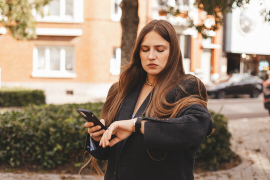 Young woman concentrating while checking her smartwatch outdoors in a casual urban setting. Modern tech lifestyle, time management and daily routine captured in warm natural light and soft colors.